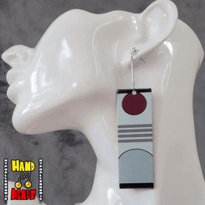 These earrings feature a vivid red rising sun, detailed with three horizontal stripes across a gray background with a grey hillside spanning the bottom of the square acrylic charm. Paired with small silver jewelry extenders and silver dropped posts.