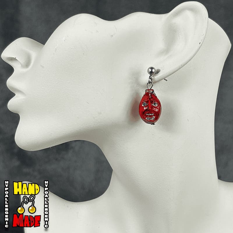 A pair of red and black anime-themed earrings displayed on a mannequin ear.