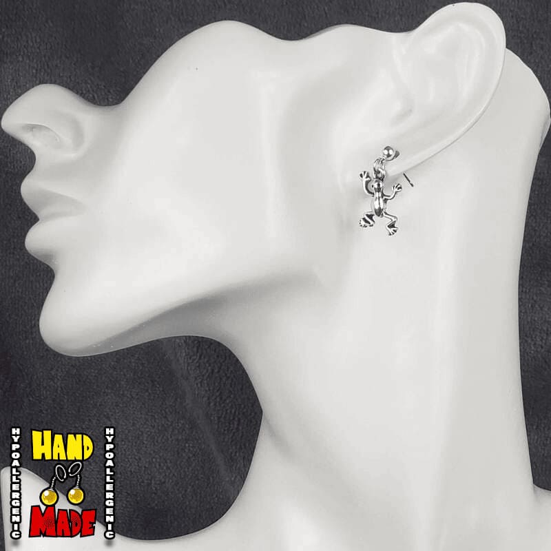A pair of silver frog charms, hanging from a silver dropped post, displayed on a mannequin head.