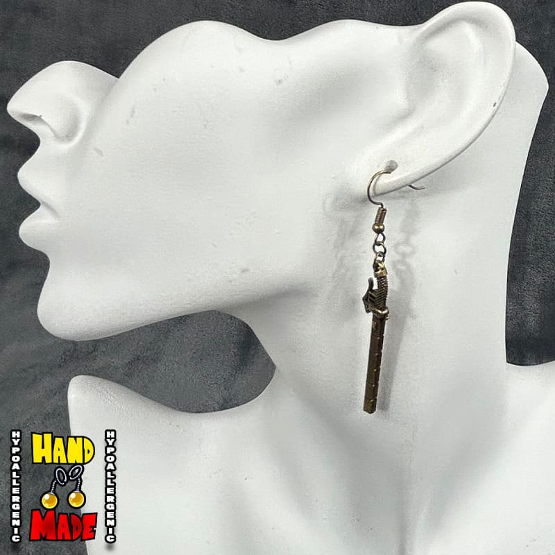 A pair of bronze metal charm earrings designed to look like gun blades, displayed on a mannequin head.