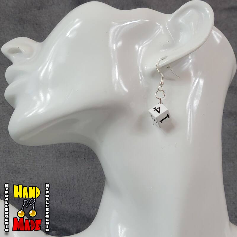 A pair of plastic white and black 6-sided dice charms, hanging from a silver French hook, displayed on a white mannequin head.