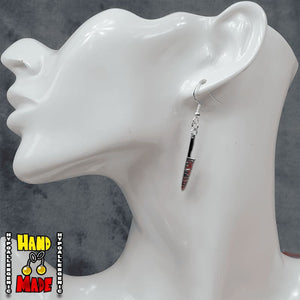 A pair of silver-colored French hook earrings with red accents designed to resemble a knife, displayed on a mannequin ear.