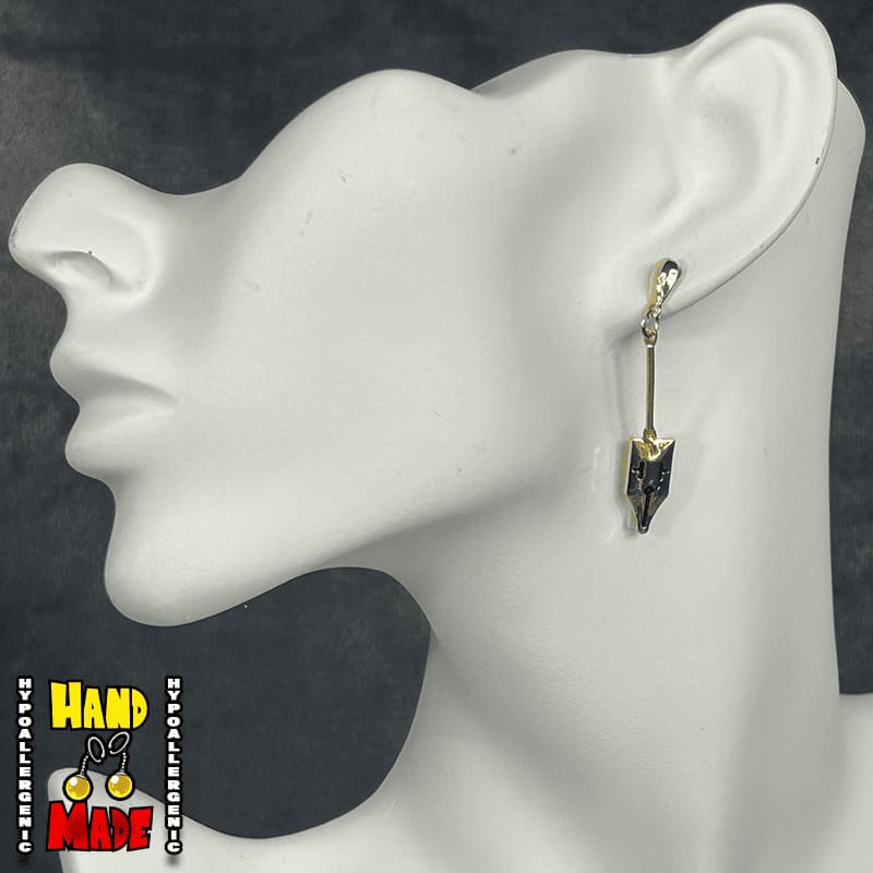A pair of dangle earrings with a golden mask design, hanging froma gold dropped post, displayed on a mannequin ear.
