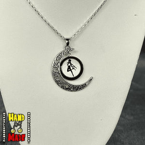 A silver-tone filigree crescent moon necklace, with a black and white charm with a dancing sailor moon displayed in the pendent, presented on a mannequin.
