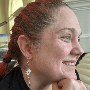 Model wearing Game Master Tome Gaming Earrings with silver book charm and hanging cudgel charm on chain.