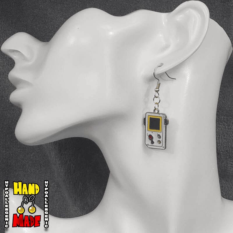 A pair of gaming earrings designed to look like a retro Gameboy with joystick, hanging from a gold French hook, displayed on a mannequin ear.