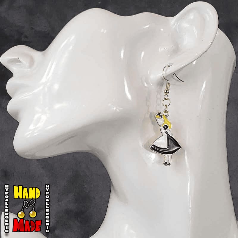 A pair of handmade gaming earrings, featuring an oversized enamel charm with a character in a black dress, resembling Alice from 'Alice in Wonderland', displayed on a mannequin ear.