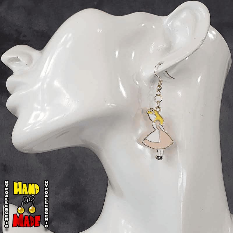 A pair of handmade gaming earrings, featuring an oversized enamel charm with a character in a pink dress, resembling Alice from 'Alice in Wonderland', displayed on a mannequin ear.