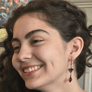 Model wearing Harlequin Jester Gaming Earrings with metal jester themed charms and silver French hooks.