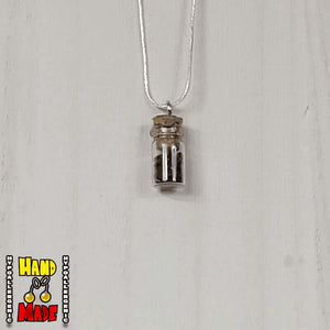 A glass jar, filled with Garnet crushed crystal, hanging from a silver necklace.