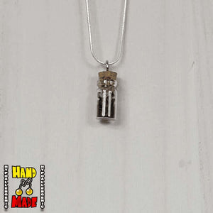 A glass jar, filled with Obsidian crushed crystal, hanging from a silver necklace.