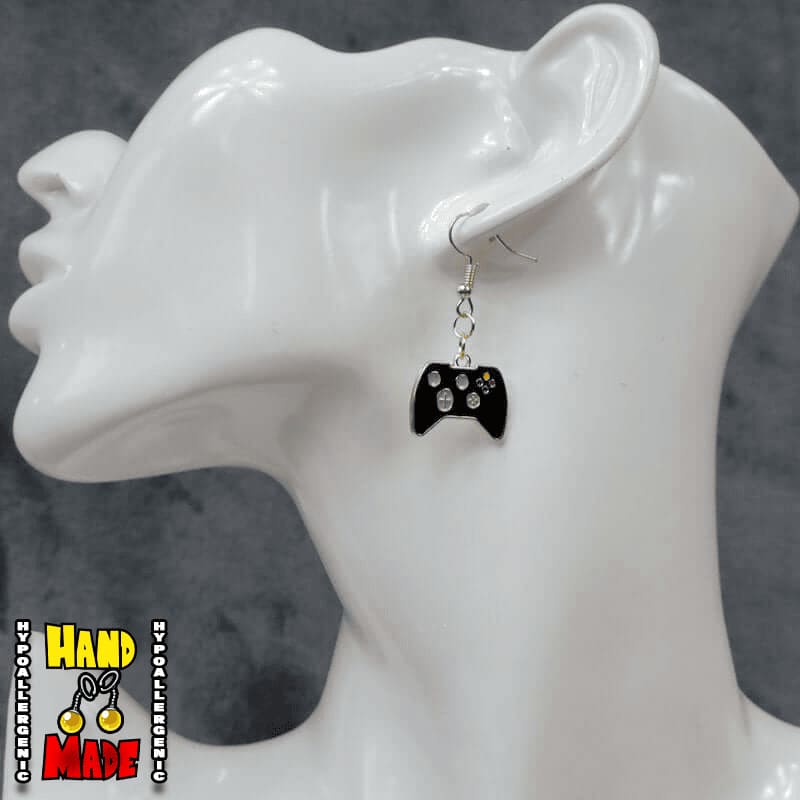 A pair of black gold painted video game controller-shaped earrings, hanging from a French hook, displayed on a white mannequin head.