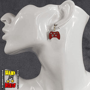 A pair of red gold painted video game controller-shaped earrings, hanging from a French hook, displayed on a white mannequin head.