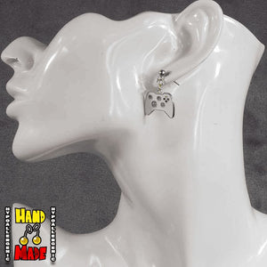 A pair of white gold painted video game controller-shaped earrings, hanging from a French hook, displayed on a white mannequin head.