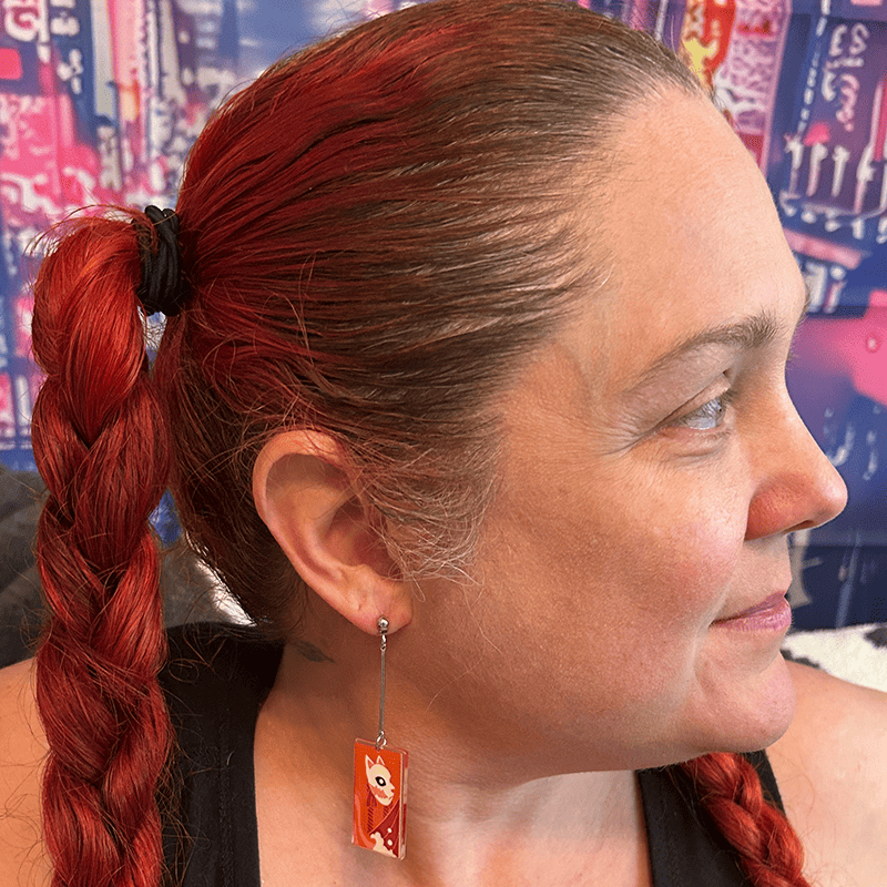 Model wearing the small Acrylic Fox Mask Hanafuda Anime Earrings, showing the bright orange acrylic charm and sterling silver dropped posts resting just below the ear.