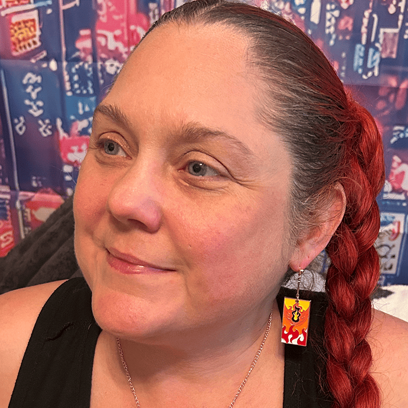 Close-up of a model wearing the Metal Fire Breathing Hanafuda Anime Earrings, showing the flame charm hanging from rose gold dropped posts against the ear