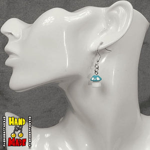 A pair of light blue and white plastic mushroom charm earrings, hanging from a silver French hook, displayed on a white mannequin head.