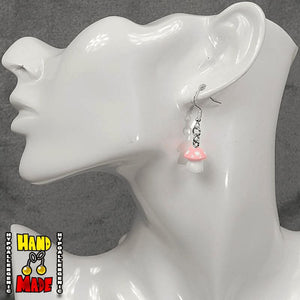 A pair of light pink and white plastic mushroom charm earrings, hanging from a silver French hook, displayed on a white mannequin head.