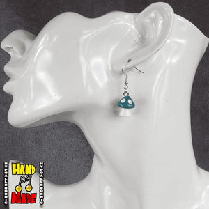 A pair of teal and white plastic mushroom charm earrings, hanging from a silver French hook, displayed on a white mannequin head.