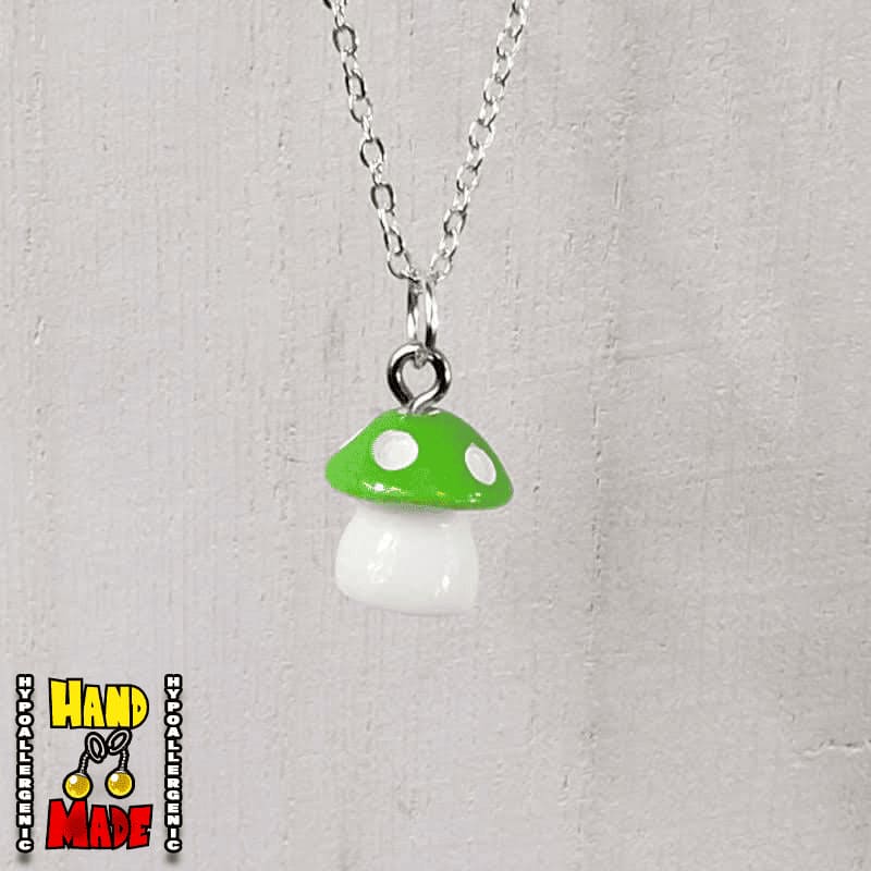 A light green and white plastic mushroom charm, hanging from a silver chain, displayed on a white board.