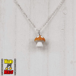 A orange and white plastic mushroom charm, hanging from a silver chain, displayed on a white board.