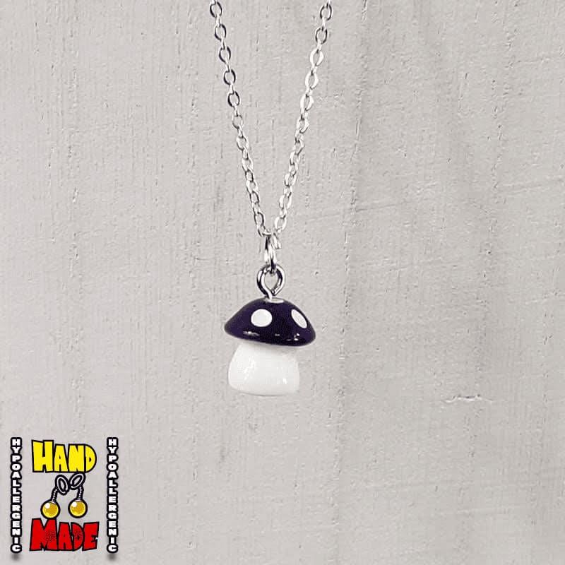 A purple and white plastic mushroom charm, hanging from a silver chain, displayed on a white board.