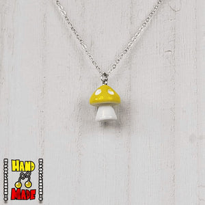 A yellow and white plastic mushroom charm, hanging from a silver chain, displayed on a white board.