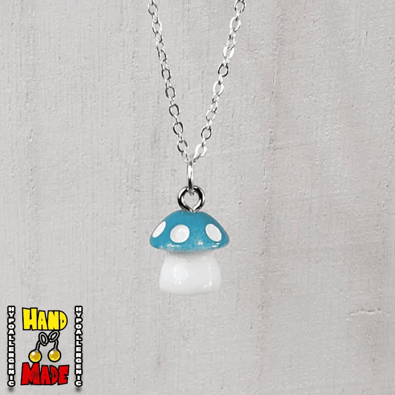 A light blue and white plastic mushroom charm, hanging from a silver chain, displayed on a white board.