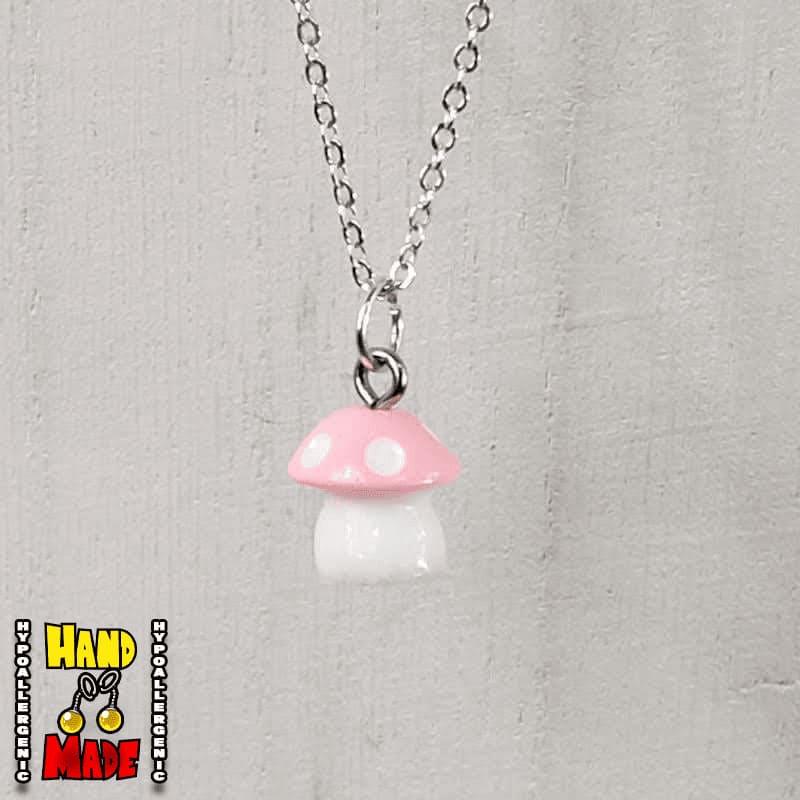 A light pink and white plastic mushroom charm, hanging from a silver chain, displayed on a white board.