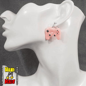 A pair of pink plastic earrings designed to resemble X-Box controllers, hanging from a silver dropped post, displayed on a mannequin head.