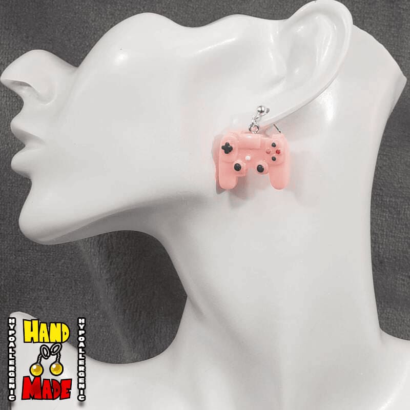 A pair of pink plastic earrings designed to resemble X-Box controllers, hanging from a silver dropped post, displayed on a mannequin head.