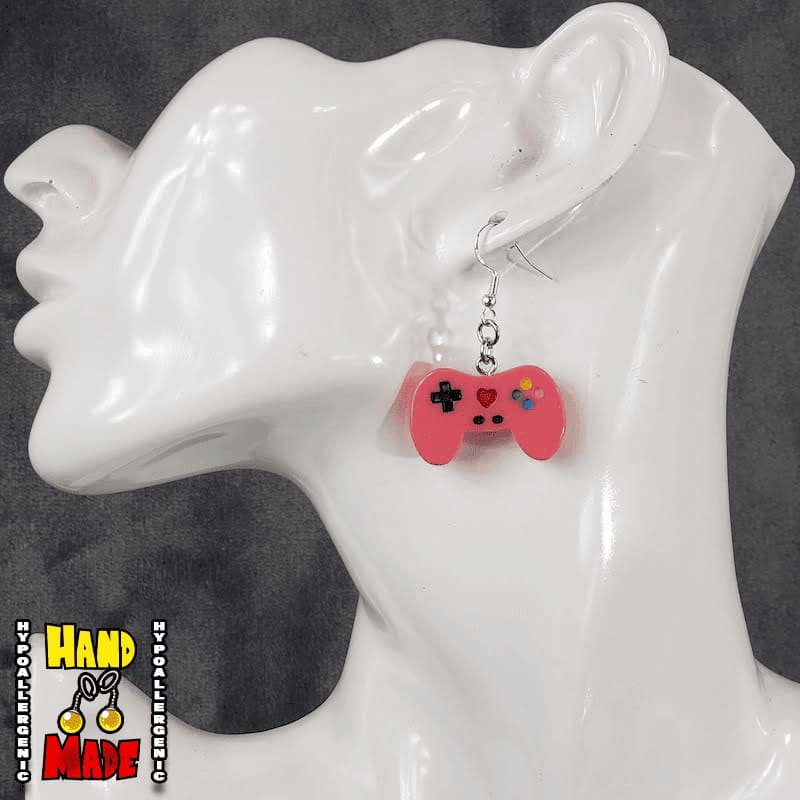 A pair of hot pink plastic video game controller-shaped earrings displayed on a mannequin head.