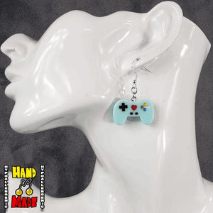 A pair of light blue plastic video game controller-shaped earrings displayed on a mannequin head.