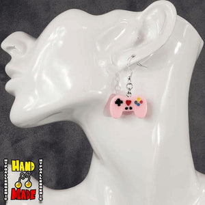 A pair of light pink plastic video game controller-shaped earrings displayed on a mannequin head.