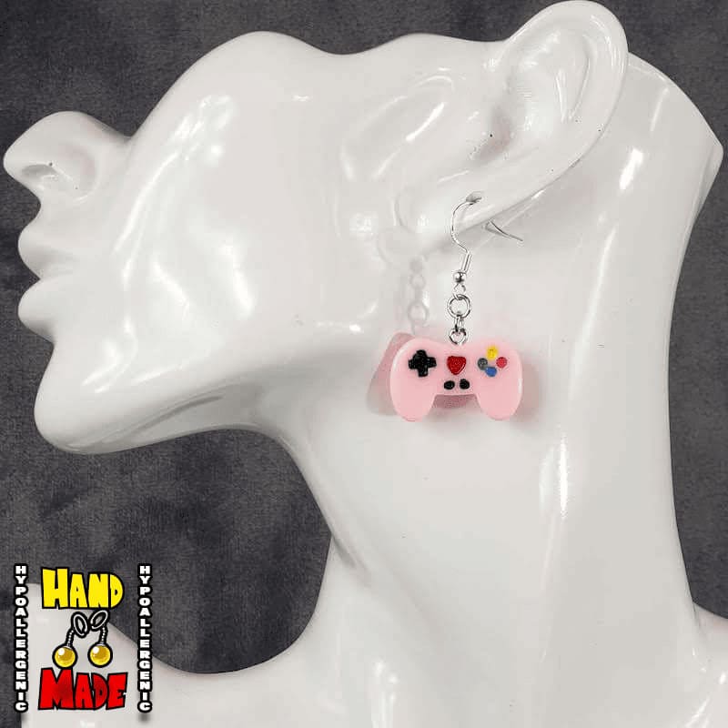 A pair of light pink plastic video game controller-shaped earrings displayed on a mannequin head.