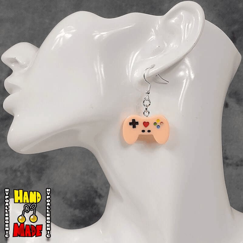 A pair of peach plastic video game controller-shaped earrings displayed on a mannequin head.