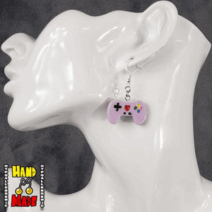 A pair of purple plastic video game controller-shaped earrings displayed on a mannequin head.