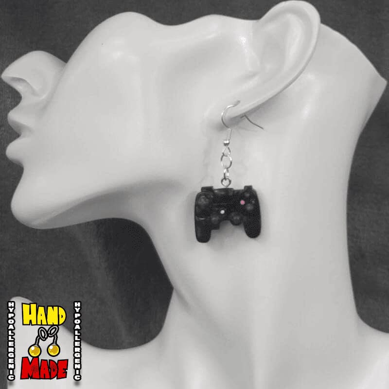 A pair of black plastic earrings designed to resemble X-Box controllers, hanging from a silver French hook, displayed on a mannequin head.