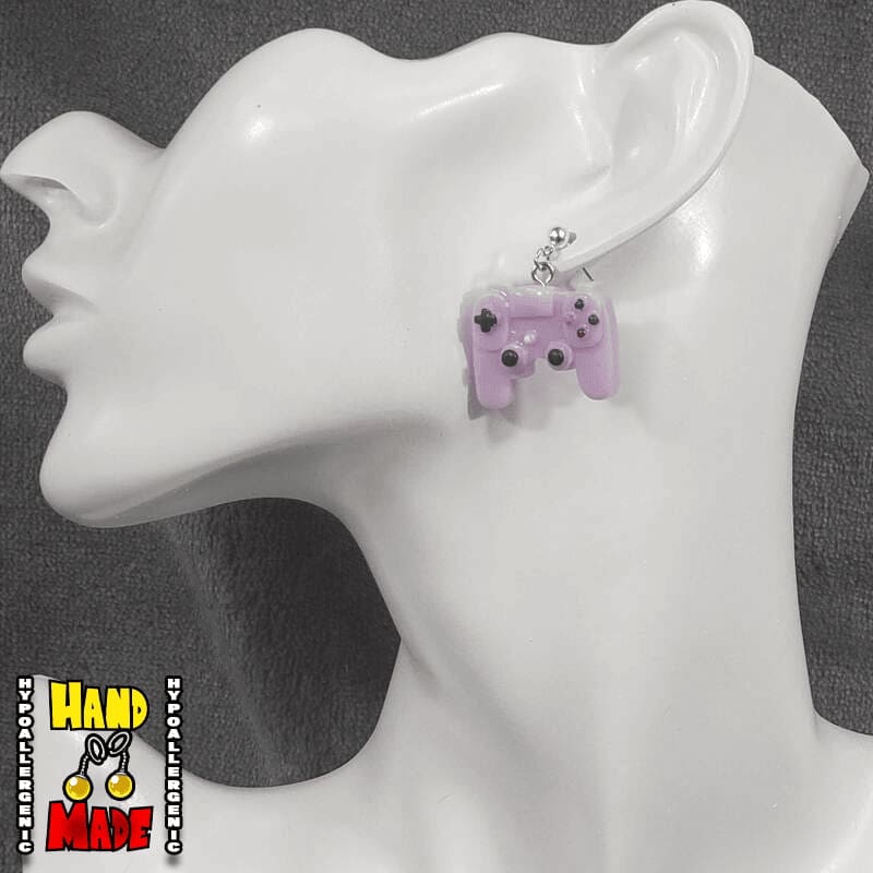 A pair of purple plastic earrings designed to resemble X-Box controllers, hanging from a silver dropped post, displayed on a mannequin head.