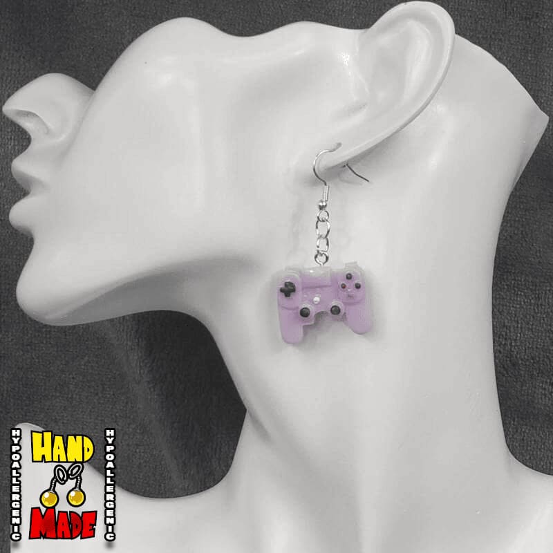A pair of purple plastic earrings designed to resemble X-Box controllers, hanging from a silver French hook, displayed on a mannequin head.