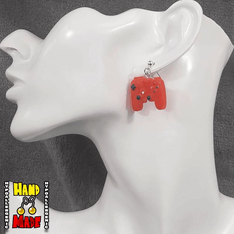 A pair of red plastic earrings designed to resemble X-Box controllers, hanging from a silver dropped post, displayed on a mannequin head.