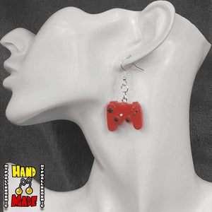 A pair of red plastic earrings designed to resemble X-Box controllers, hanging from a silver French hook, displayed on a mannequin head.