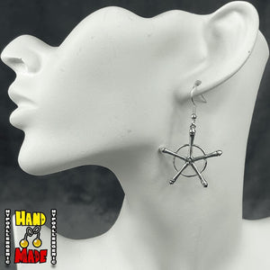 A pair of silver-colored earrings, designed with a star helm charm, hanging from a silver French hook, displayed on a mannequin ear.