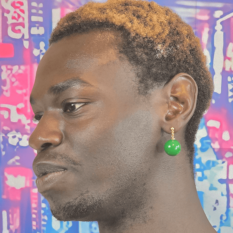 Model wearing Emerald Ascension Anime Earrings with glossy green sphere charms and gold dropped posts.
