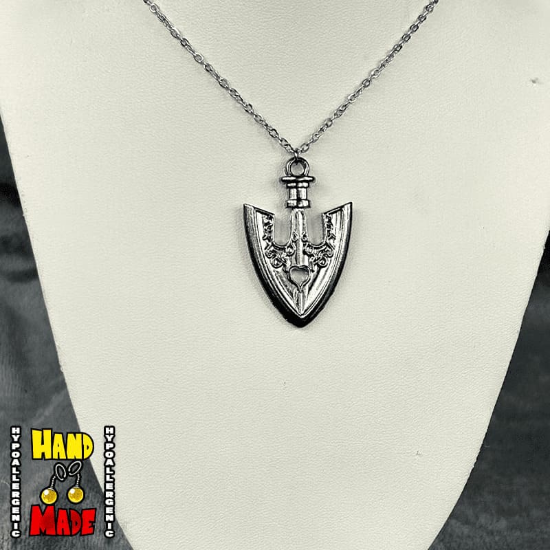 A metal silver arrowhead charm, hanging from a silver necklace, displayed on a white background.