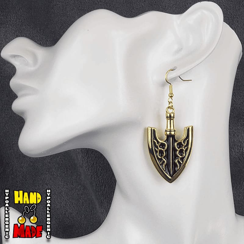 A pair of gold-colored arrowhead earrings, hanging from a gold French hook, displayed on a mannequin head.