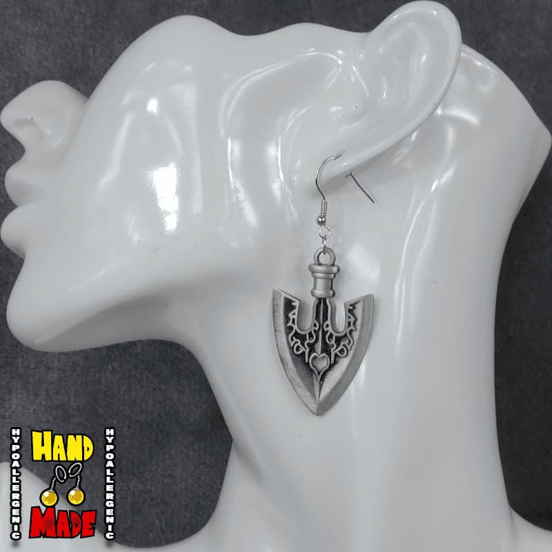 A pair of silver-colored arrowhead earrings, hanging from a silver French hook, displayed on a mannequin head.