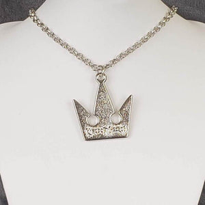 A silver-colored crown-shaped necklace on a mannequin bust, featuring a silver chain.