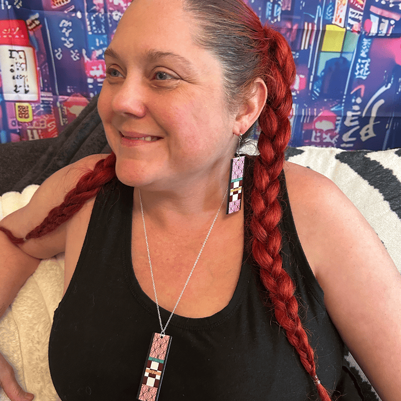 A person wearing a black top and showcasing a silver-colored necklace with a rectangular acrylic pendant featuring pink and green colors.