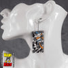 A pair of acrylic earrings with a geometric snake pattern in black, white, yellow, and blue, displayed on a mannequin head.